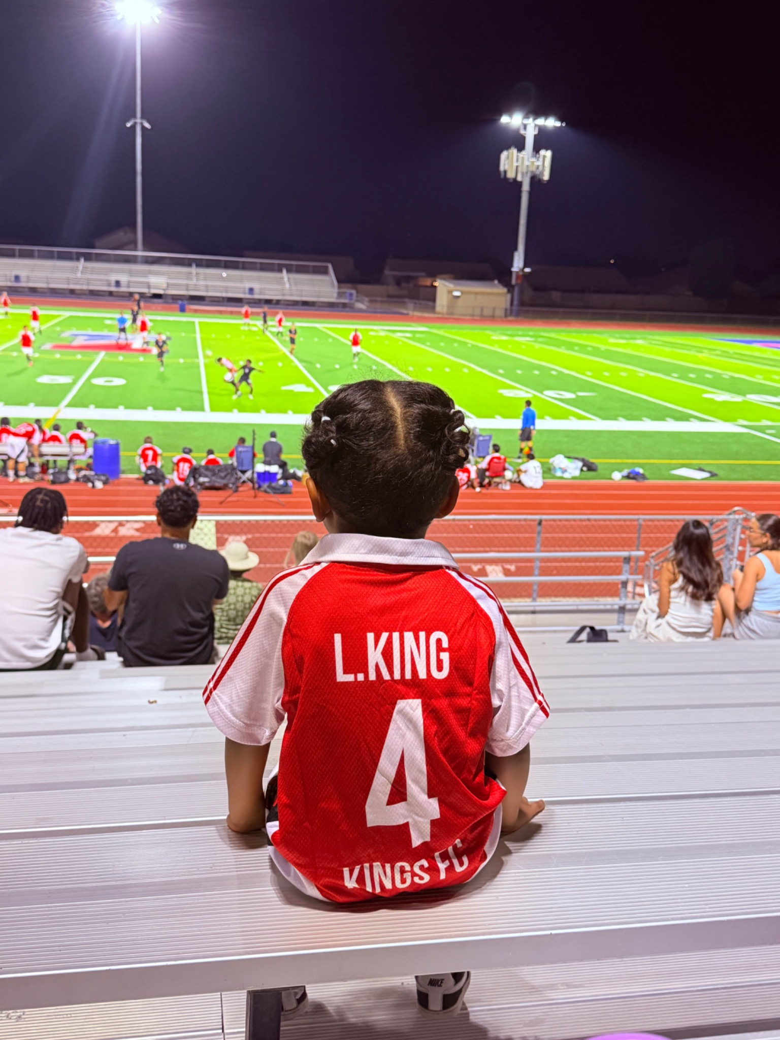 A young Kings FC supporter watching the pitch from the stands.