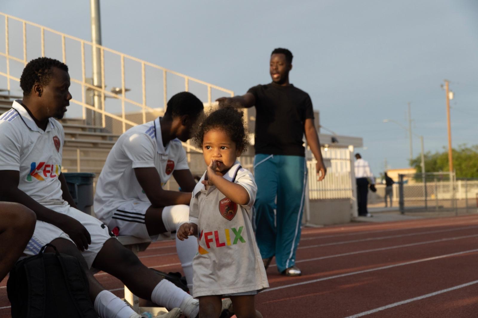 A young supporter beside Kings FC players on the touchline.